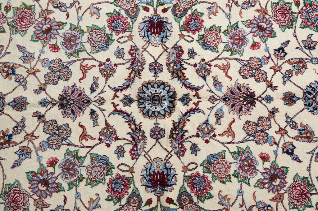 A close-up of an ornate floral patterned rug or textile with a cream background and intricate motifs in blue, pink, red, green, and brown.