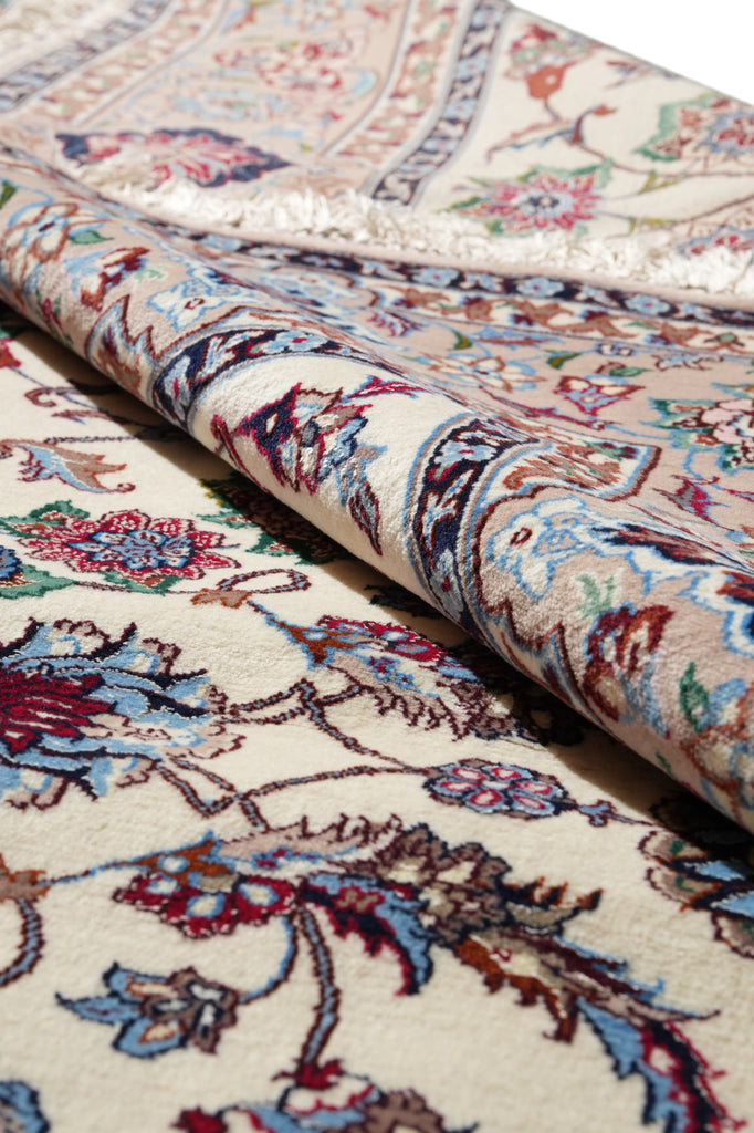 A close-up of a folded traditional oriental rug showing its detailed floral pattern in cream, beige, blue, red, and brown tones.