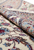 Load image into Gallery viewer, A close-up of a folded traditional oriental rug showing its detailed floral pattern in cream, beige, blue, red, and brown tones.
