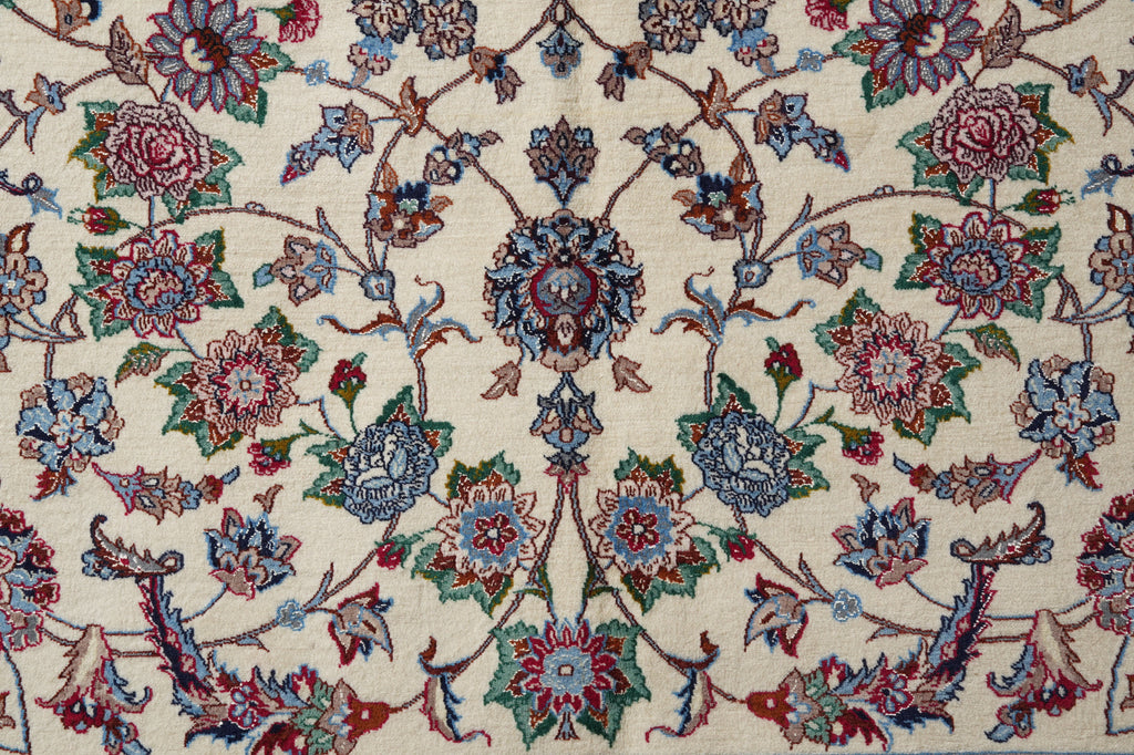 A close-up of an ornate floral patterned rug or textile on a cream background, featuring blue, red, green, and brown botanical motifs.