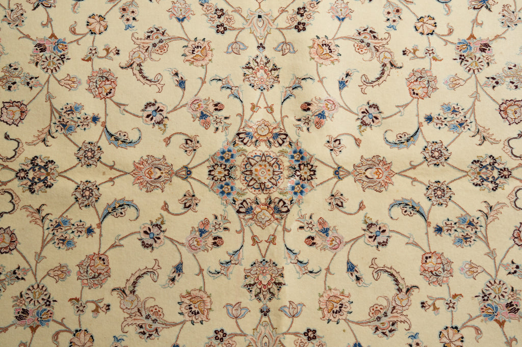 A close-up of an ornate Persian-style rug with a cream background and intricate floral motifs in dusty pink, blue, and brown.