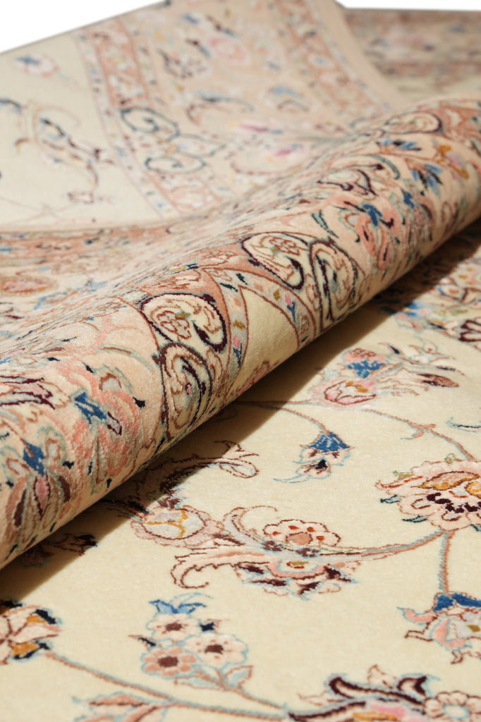 A close-up of a rolled area rug showing its detailed floral and paisley pattern in beige, pink, blue, and brown tones.