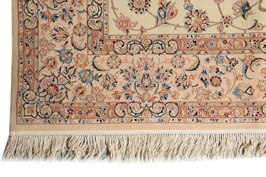 Close-up of a traditional patterned rug corner showing floral motifs, ornate borders, and cream fringe on a white background.
