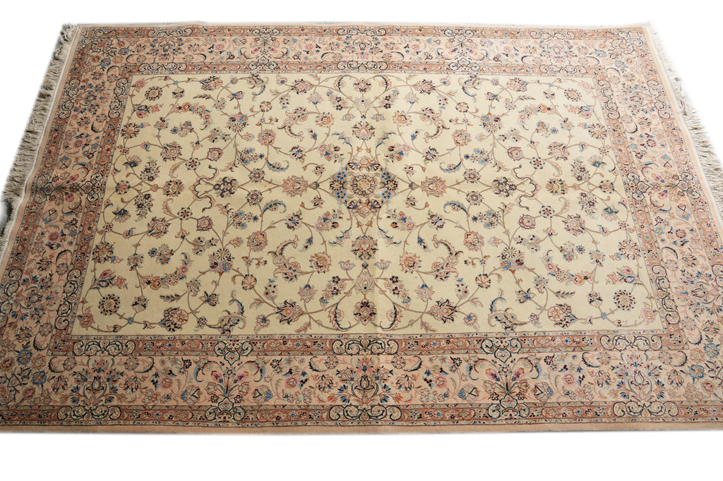 A rectangular traditional area rug with an intricate floral and vine pattern, featuring a cream center field, a dusty pink border, and blue and green accents, shown flat against a white background.