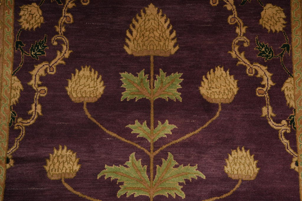 Close-up of a woven textile or rug featuring a botanical pattern with tan thistle-like flowers, green leaves, and ornate gold vine motifs on a deep purple background.