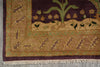 Load image into Gallery viewer, Close-up of a woven rug corner showing a dark plum purple field with a green plant motif, a tan border with leaf patterns, and cream fringe.
