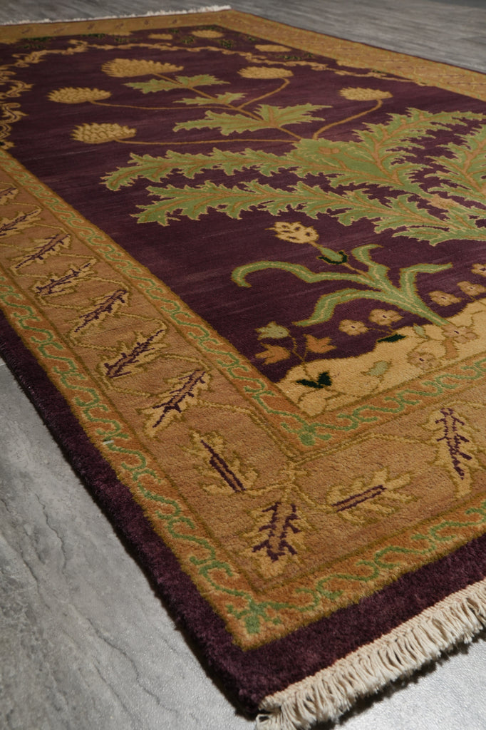 A close-up of a traditional area rug with a deep burgundy field, a wide tan border, and green floral motifs, laid out on a gray stone floor.