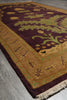 Load image into Gallery viewer, A close-up of a traditional area rug with a deep burgundy field, a wide tan border, and green floral motifs, laid out on a gray stone floor.