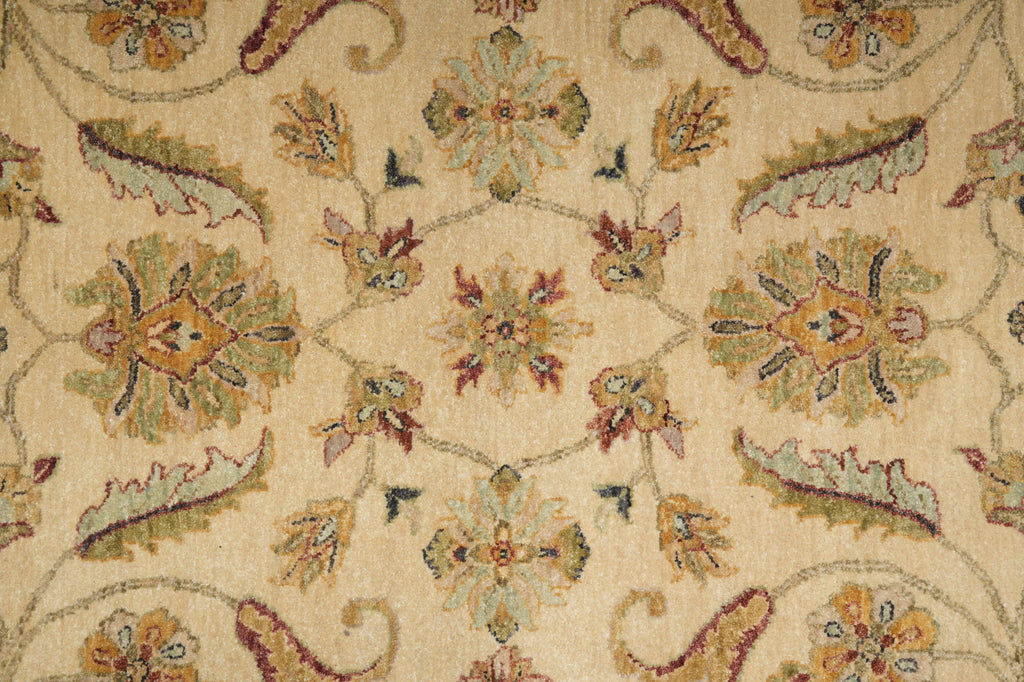 A close-up of a traditional patterned rug with a beige background and ornate floral motifs in muted green, yellow, and burgundy.