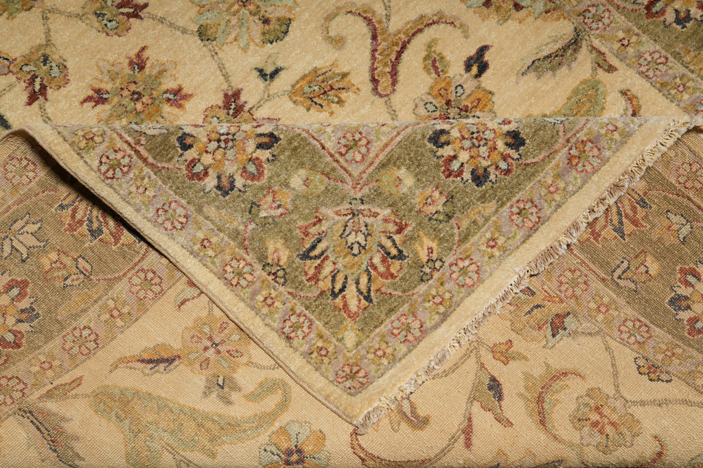 A close-up of a folded patterned rug showing its intricate floral and paisley design in beige, olive green, and muted red tones.