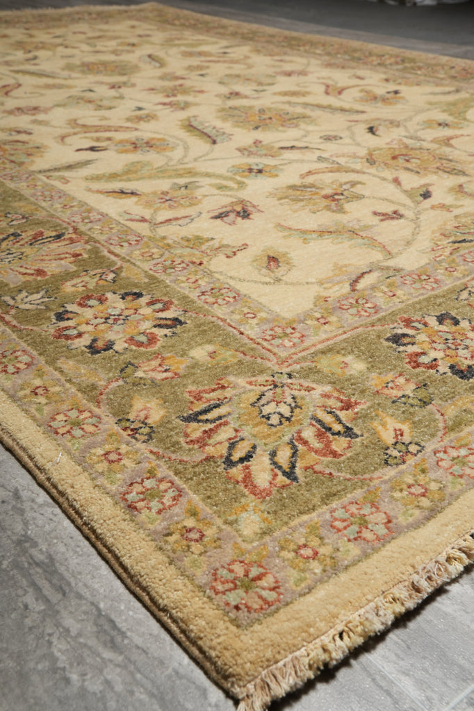 A close-up view of a traditional oriental area rug with a cream and olive green base, featuring floral motifs and a patterned border, laid out on a gray concrete floor.
