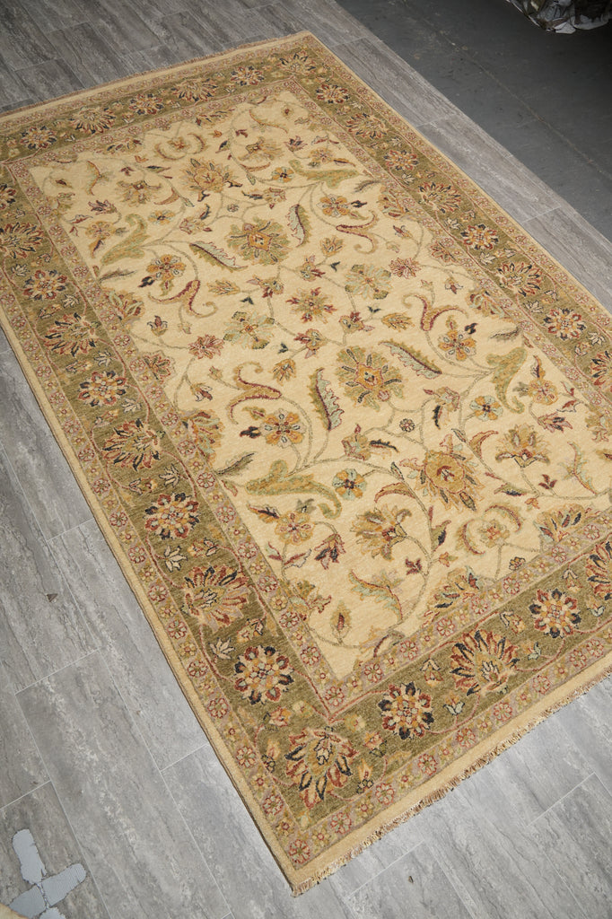 An ornate rectangular area rug with a beige center and detailed floral motifs, laid out diagonally on a gray wood-plank floor.