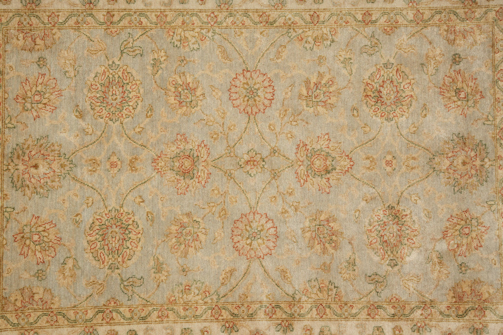 An ornate traditional area rug with a floral pattern in muted tones of beige, dusty blue, and terracotta red.