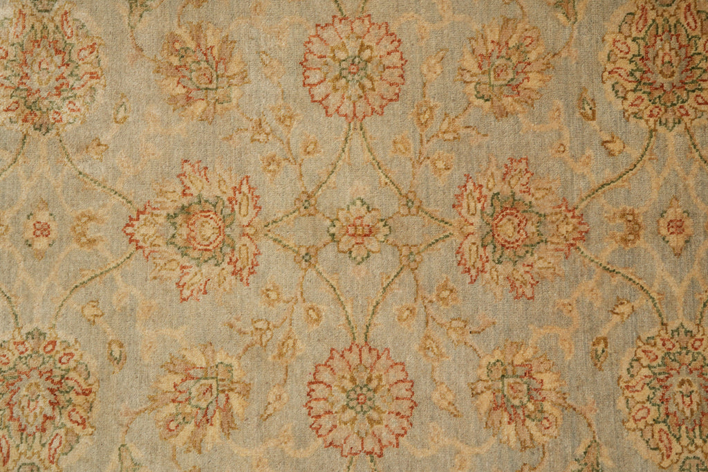 A close-up of a woven textile or rug pattern with a repeating floral motif in muted red, beige, and green on a light gray-beige ground.
