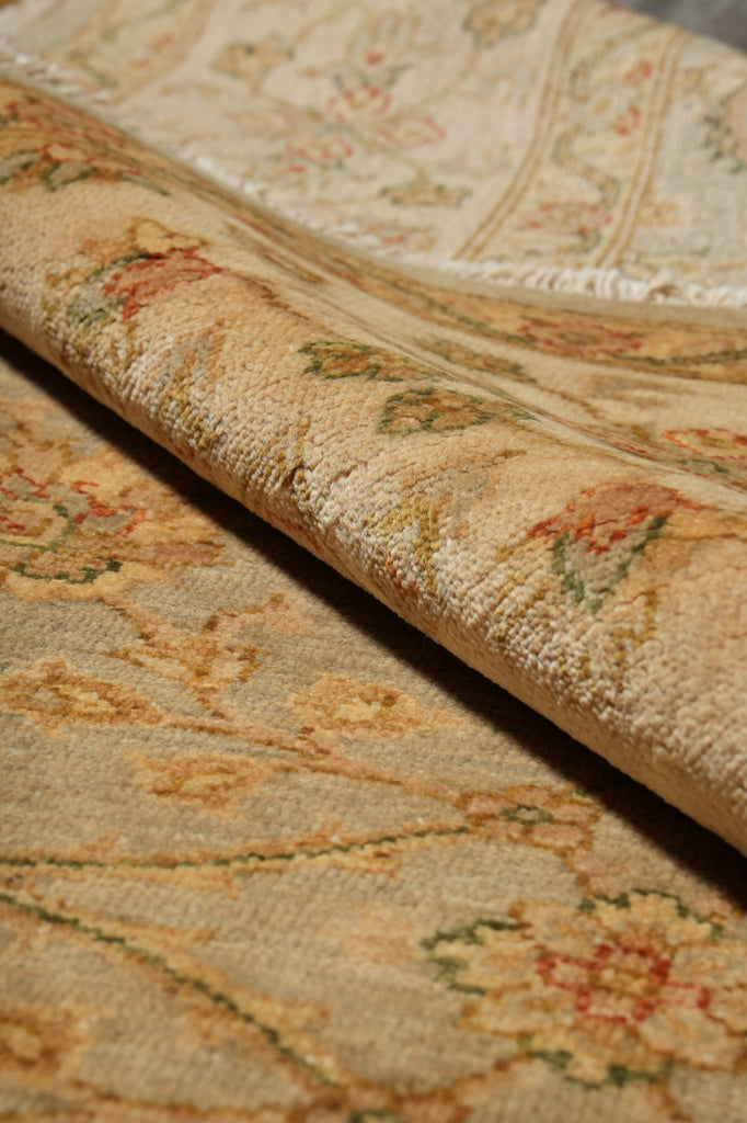 A close-up of a folded area rug showing its detailed floral pattern in beige, gold, and muted green tones.