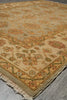Load image into Gallery viewer, A close-up of a traditional patterned area rug with a beige base, featuring floral motifs in muted orange, green, and red, with a fringed edge on a gray concrete floor.