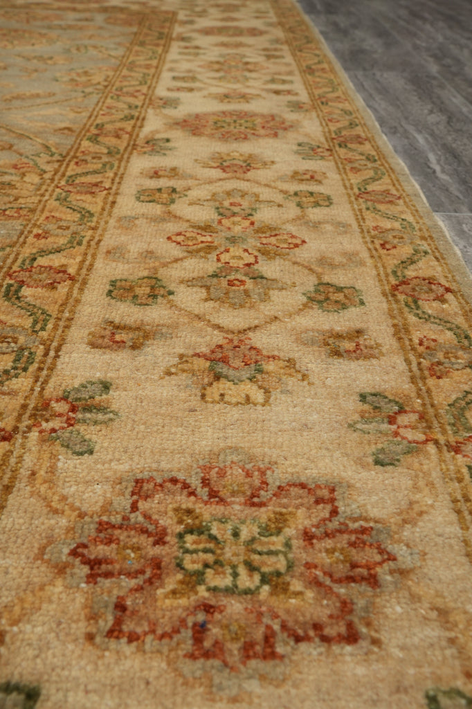 A close-up view of a traditional area rug with a beige base and a detailed floral pattern in muted red, green, and gold tones, laid out on a gray floor.