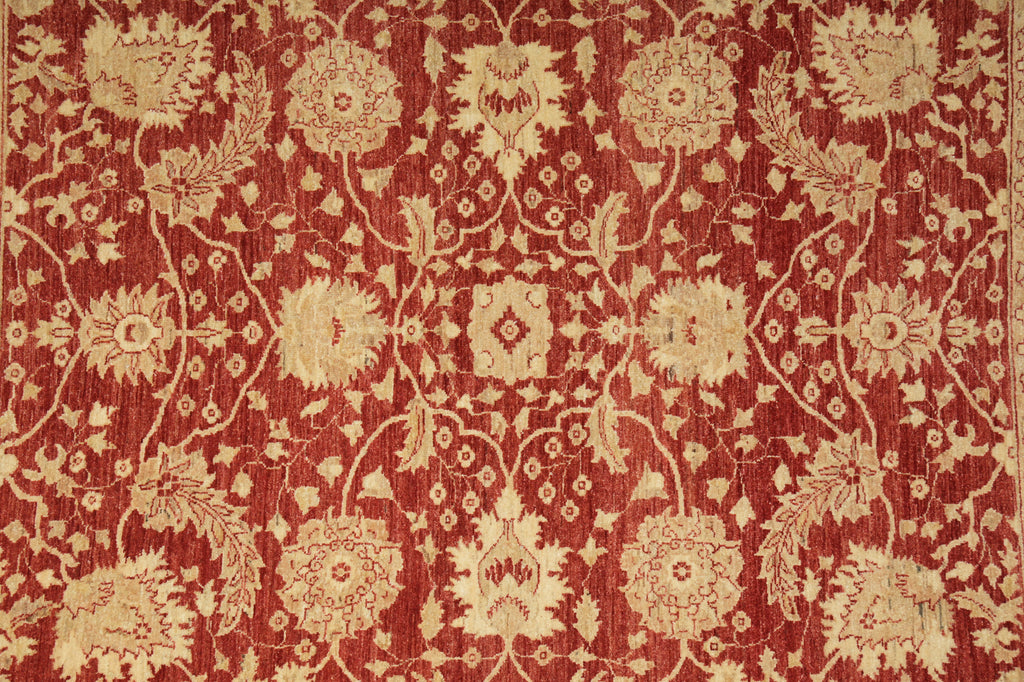 A close-up of a red and beige floral patterned rug or textile, showing an ornate repeating botanical design with cream-colored motifs on a rust-red background.