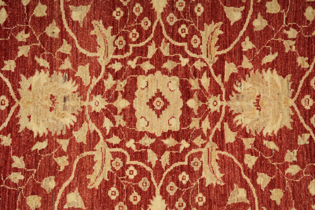 A close-up of a traditional patterned rug featuring a deep red background with beige floral and vine motifs.