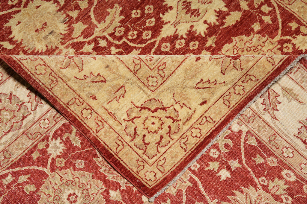 A close-up of an ornate area rug showing its corner detail, featuring a traditional floral and vine pattern in red and beige.
