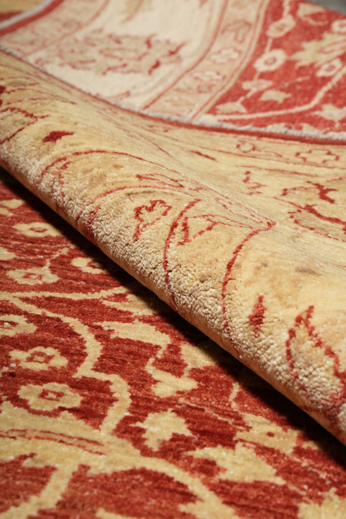 A close-up of a folded area rug showing its cream and rust-red patterned pile and woven texture.