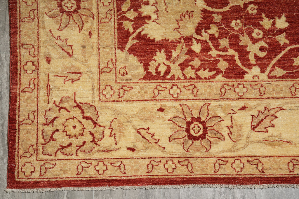 Close-up of a traditional patterned rug corner showing a cream and rust red floral design with a decorative border.