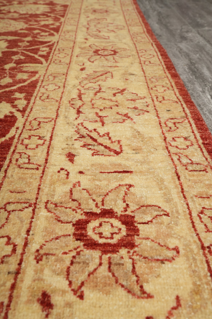 A close-up view of a traditional patterned area rug with a warm beige background and red floral motifs, shown on a gray floor.
