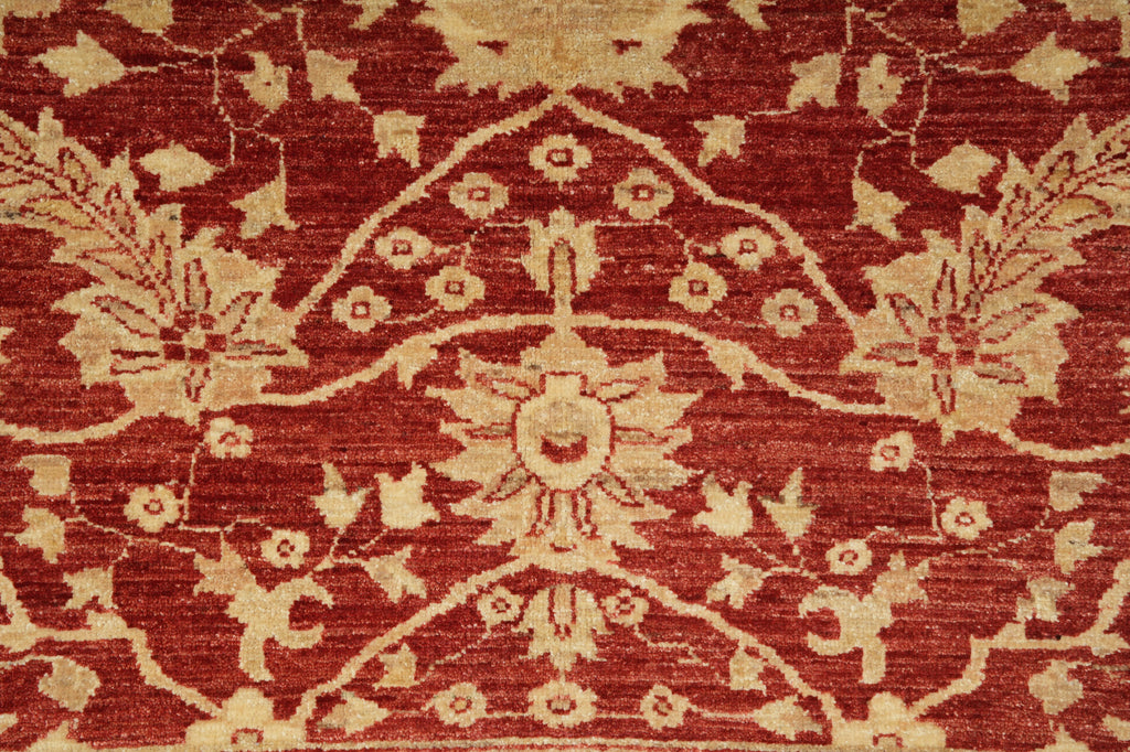 A close-up of a traditional patterned rug featuring a deep red background with beige floral and botanical motifs.
