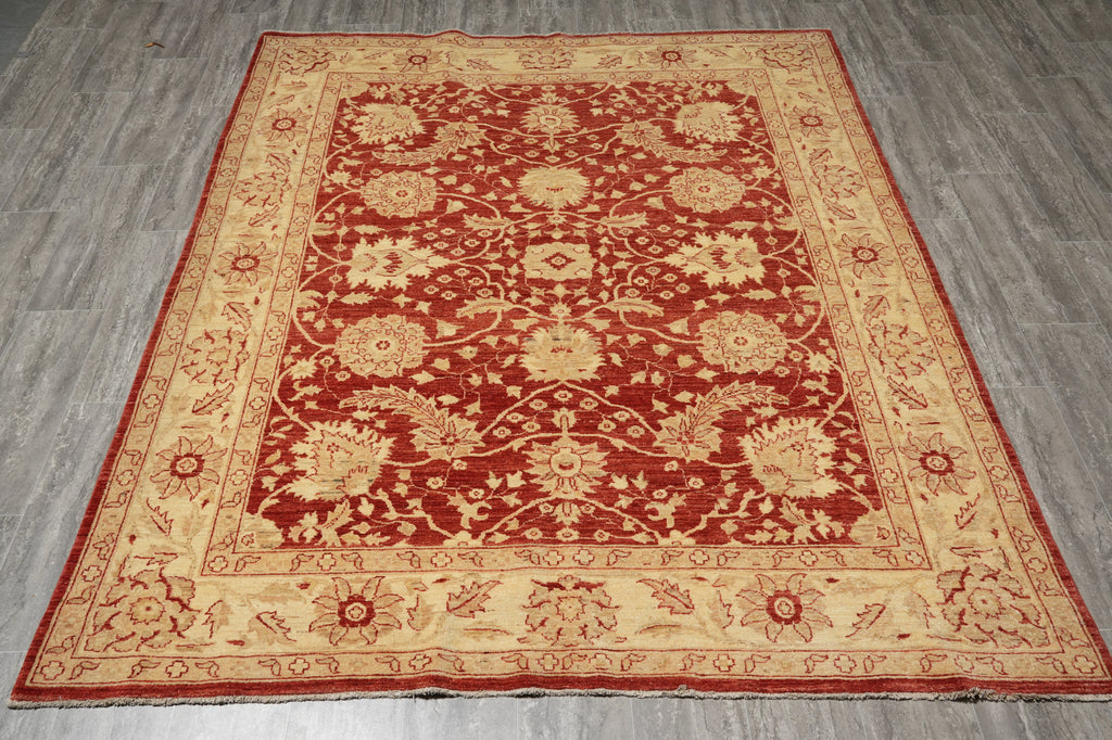 A rectangular traditional area rug with a red field and beige floral motifs, laid flat on a gray wood-look floor.