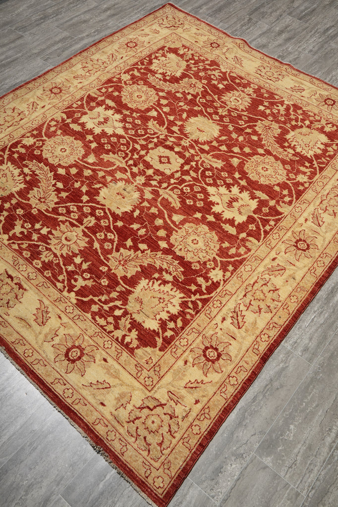 A traditional oriental area rug with a red field and beige floral motifs, laid out on a gray wood-look floor.