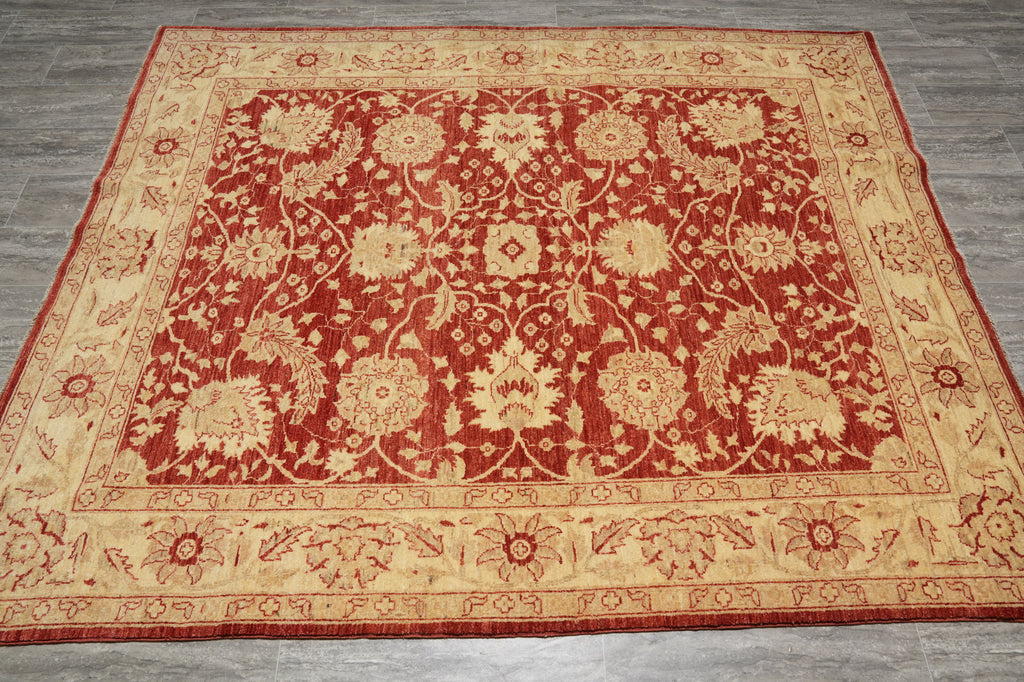 A rectangular traditional area rug with an ornate floral and medallion pattern, featuring a deep red center field and a wide beige border, laid flat on a gray wood floor.