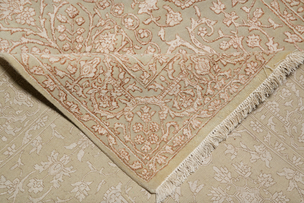 A close-up of a beige and cream patterned rug, showing the corner with fringed edges and detailed floral motifs.