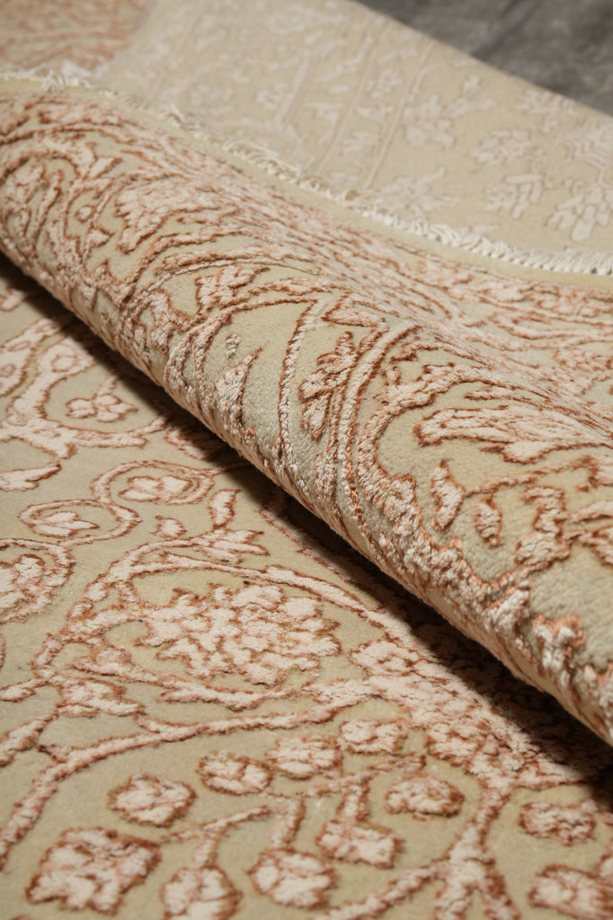 A close-up of a beige and tan patterned rug with a rolled section showing the raised floral and vine texture.