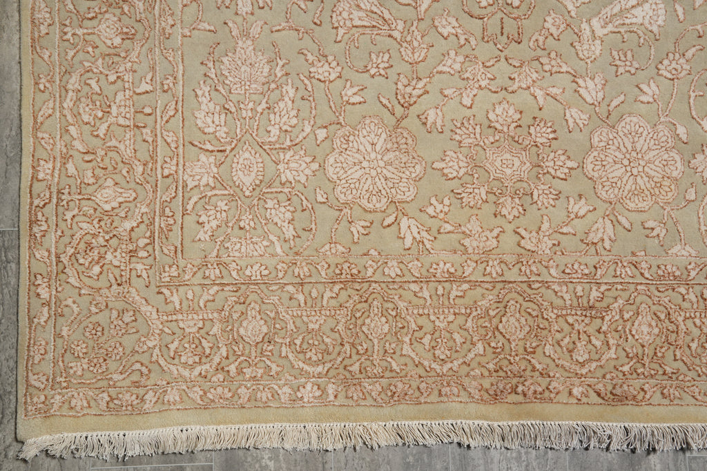 Close-up of an ornate area rug showing its detailed floral pattern and fringed edge, in muted beige and dusty rose tones.