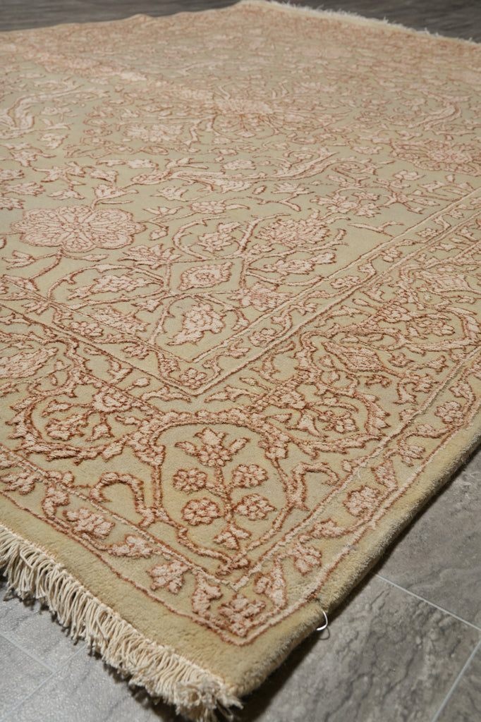 A close-up of a traditional area rug with a beige base and dusty rose floral patterns, laid out on a gray tiled floor.