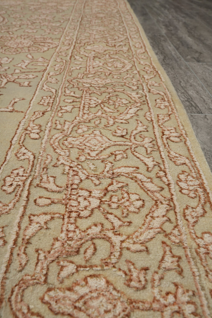 A close-up view of a traditional patterned area rug with a beige base and dusty rose floral motifs, laid out on a gray wood floor.