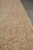 Load image into Gallery viewer, A close-up view of a traditional patterned area rug with a beige base and dusty rose floral motifs, laid out on a gray wood floor.