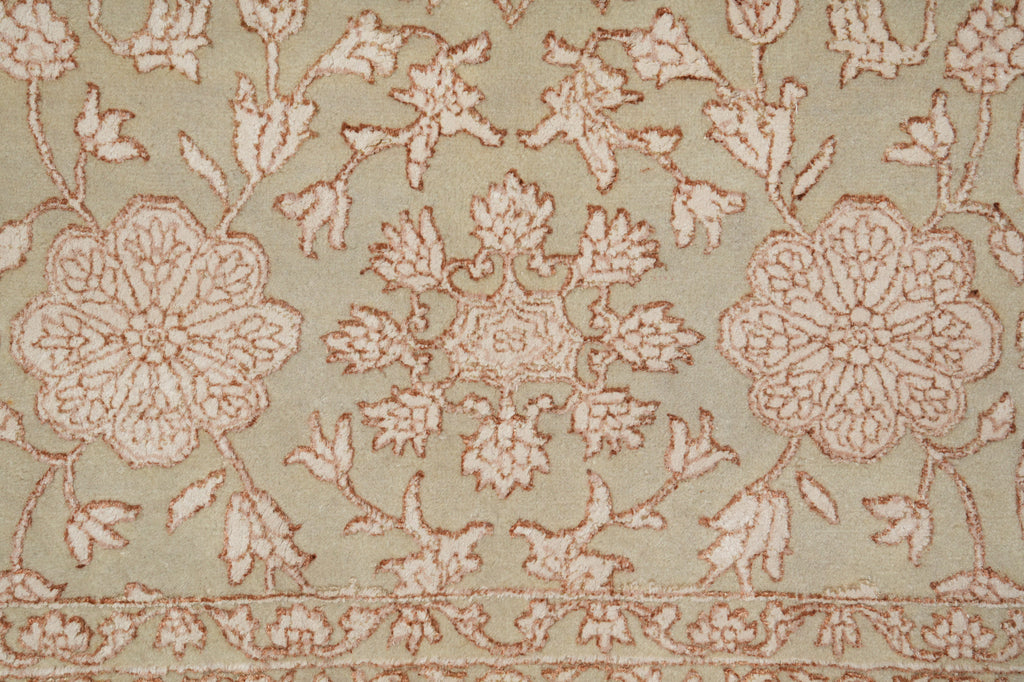 A close-up of a traditional patterned rug featuring a central medallion and floral motifs in dusty pink and beige on a muted sage green background.