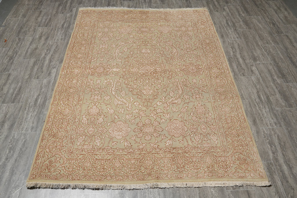 A rectangular area rug with a traditional floral pattern in muted beige, pink, and light green tones, laid flat on a gray wood-look floor.