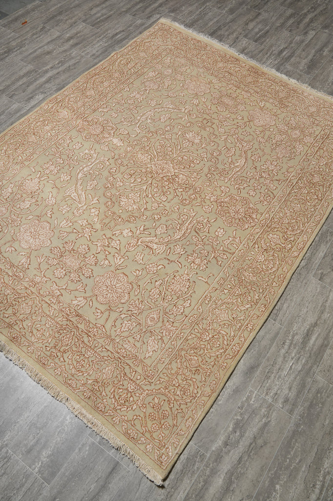A rectangular area rug with an intricate floral and botanical pattern in beige and muted pink, laid out on a gray wood-look floor.