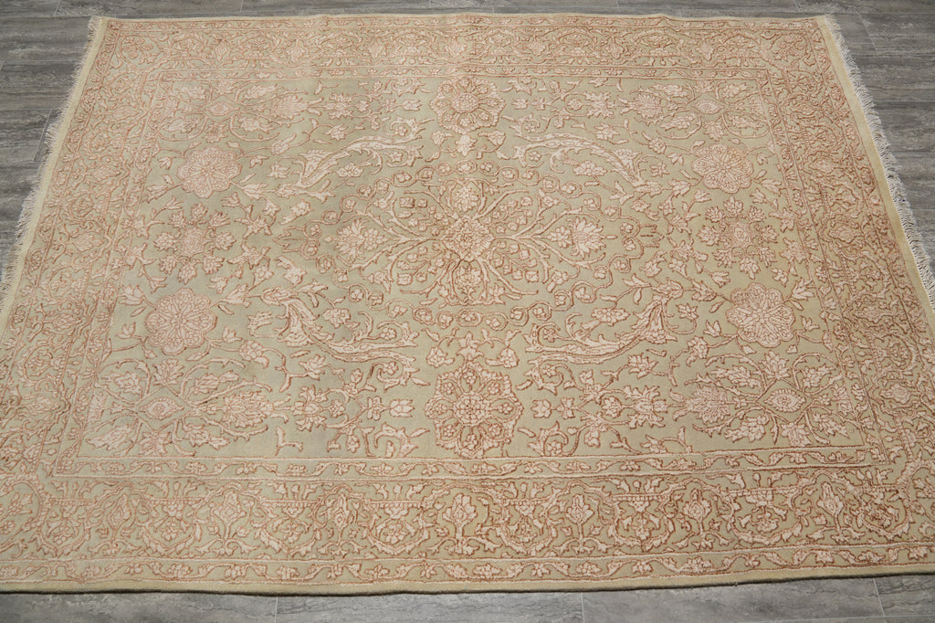 A square area rug with an intricate floral and medallion pattern in muted beige and dusty rose tones, laid flat on a gray wood floor.
