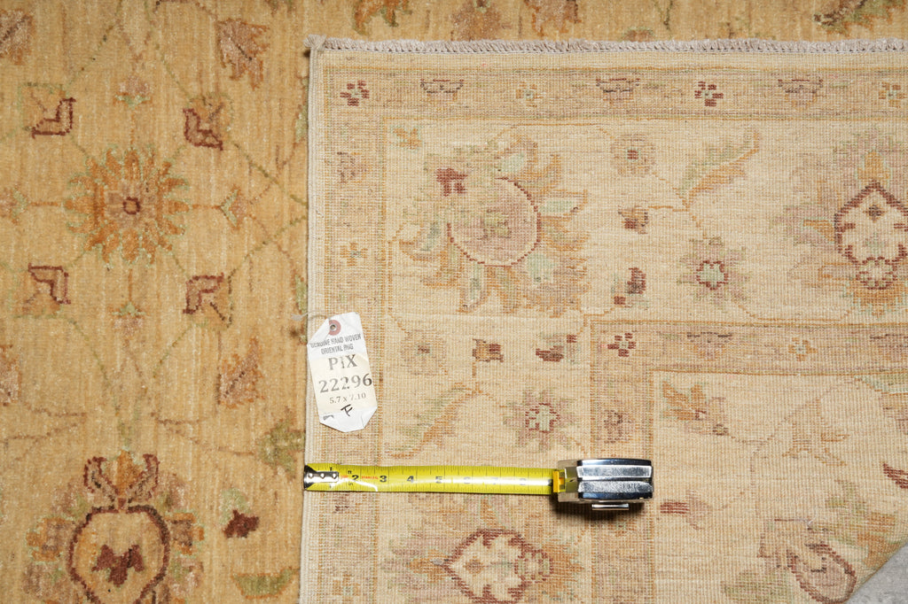 A folded beige patterned rug laid flat on a matching rug, with a yellow tape measure placed horizontally to indicate size. A small white tag is attached near the center.