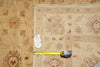 Load image into Gallery viewer, A folded beige patterned rug laid flat on a matching rug, with a yellow tape measure placed horizontally to indicate size. A small white tag is attached near the center.