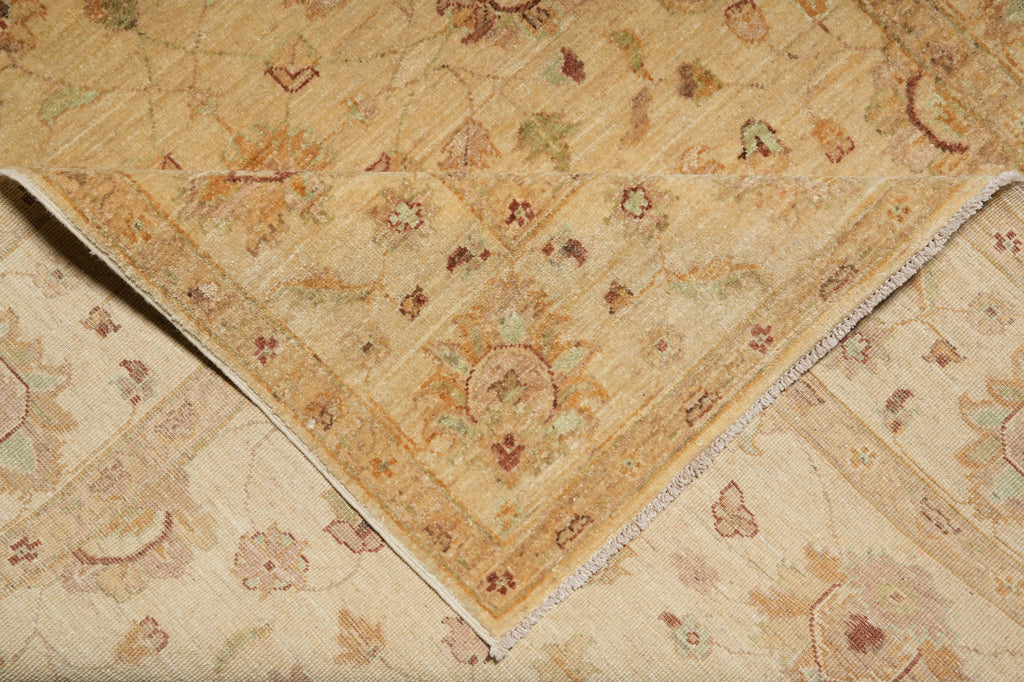 A close-up of a traditional patterned area rug with a folded corner showing its texture and fringed edge. The rug features a warm beige and cream base with intricate floral motifs in muted brown, green, and rust tones.
