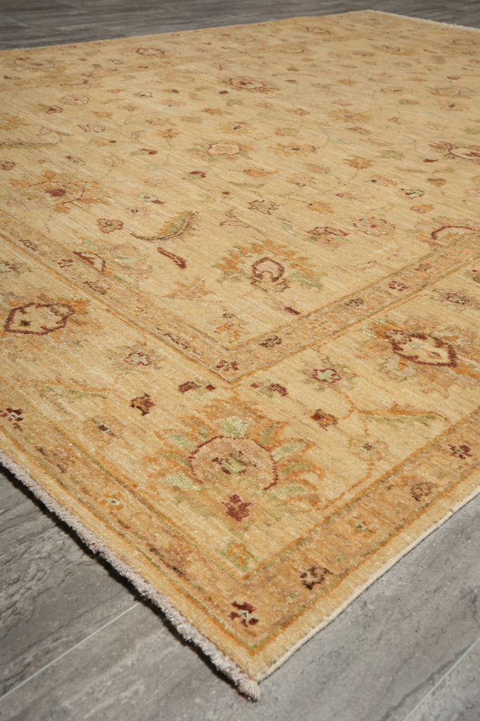A traditional area rug with a warm beige and golden-yellow base, featuring faded floral and geometric motifs in muted brown, green, and rust tones, shown laid out on a gray wood floor.