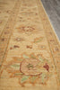 Load image into Gallery viewer, A close-up view of a traditional area rug with a warm beige base and faded floral motifs in muted green, brown, and rust tones, shown on a dark wood floor.