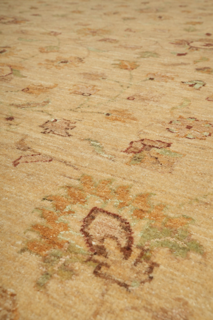 A close-up view of a traditional area rug with a warm beige base and faded floral motifs in muted orange, brown, and soft green.