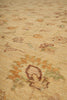 Load image into Gallery viewer, A close-up view of a traditional area rug with a warm beige base and faded floral motifs in muted orange, brown, and soft green.