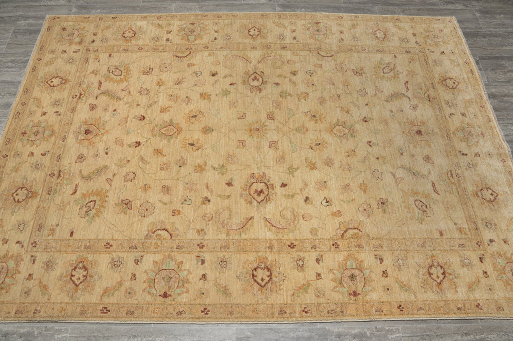 A large rectangular area rug with an intricate traditional floral and medallion pattern in warm beige, tan, and muted brown tones, laid out on a gray tiled floor.