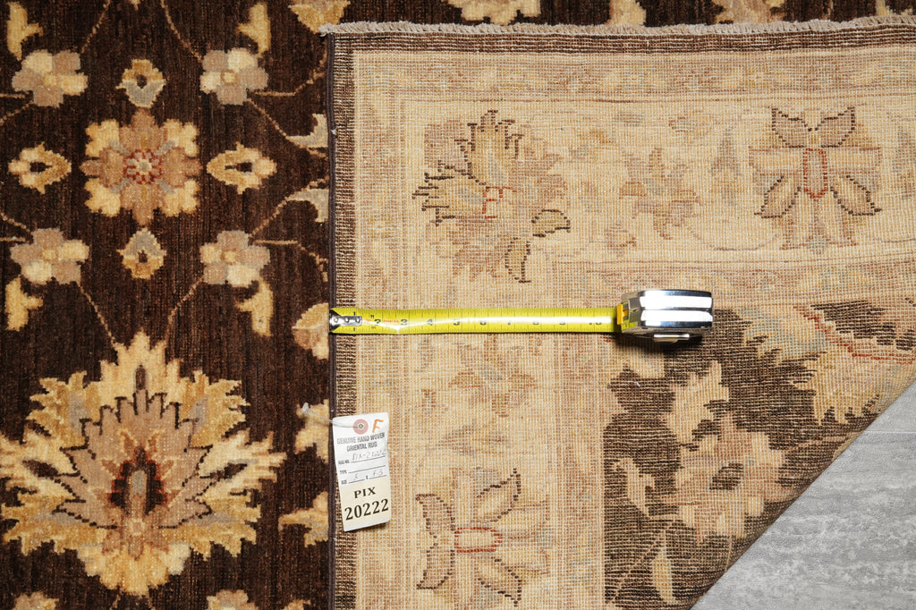 A close-up of a traditional oriental rug with a dark brown floral pattern on the left and a beige section on the right, shown with a yellow tape measure and a price tag.